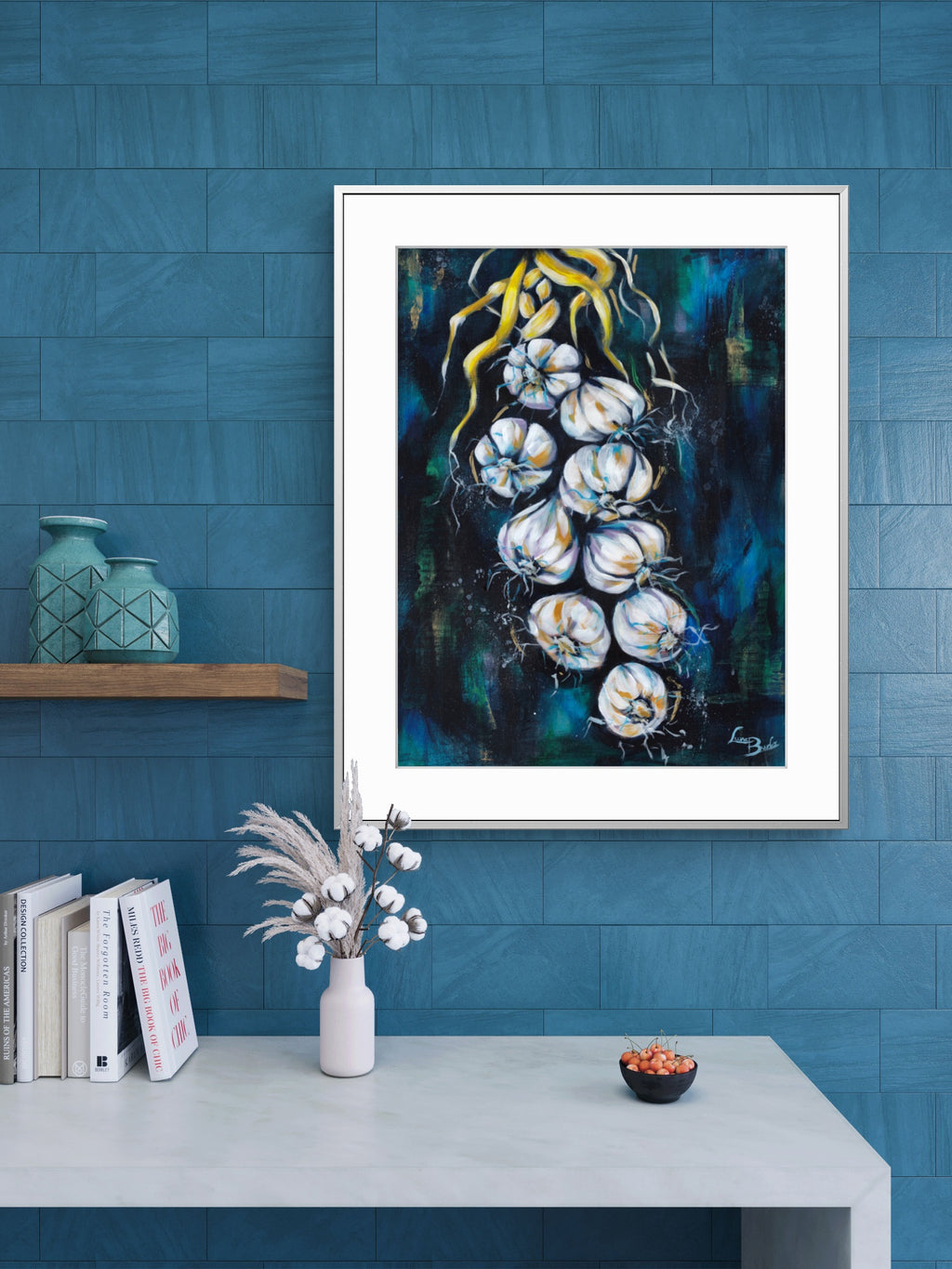Framed Luna Burlo artwork of white garlic on a blue wall with decor items below