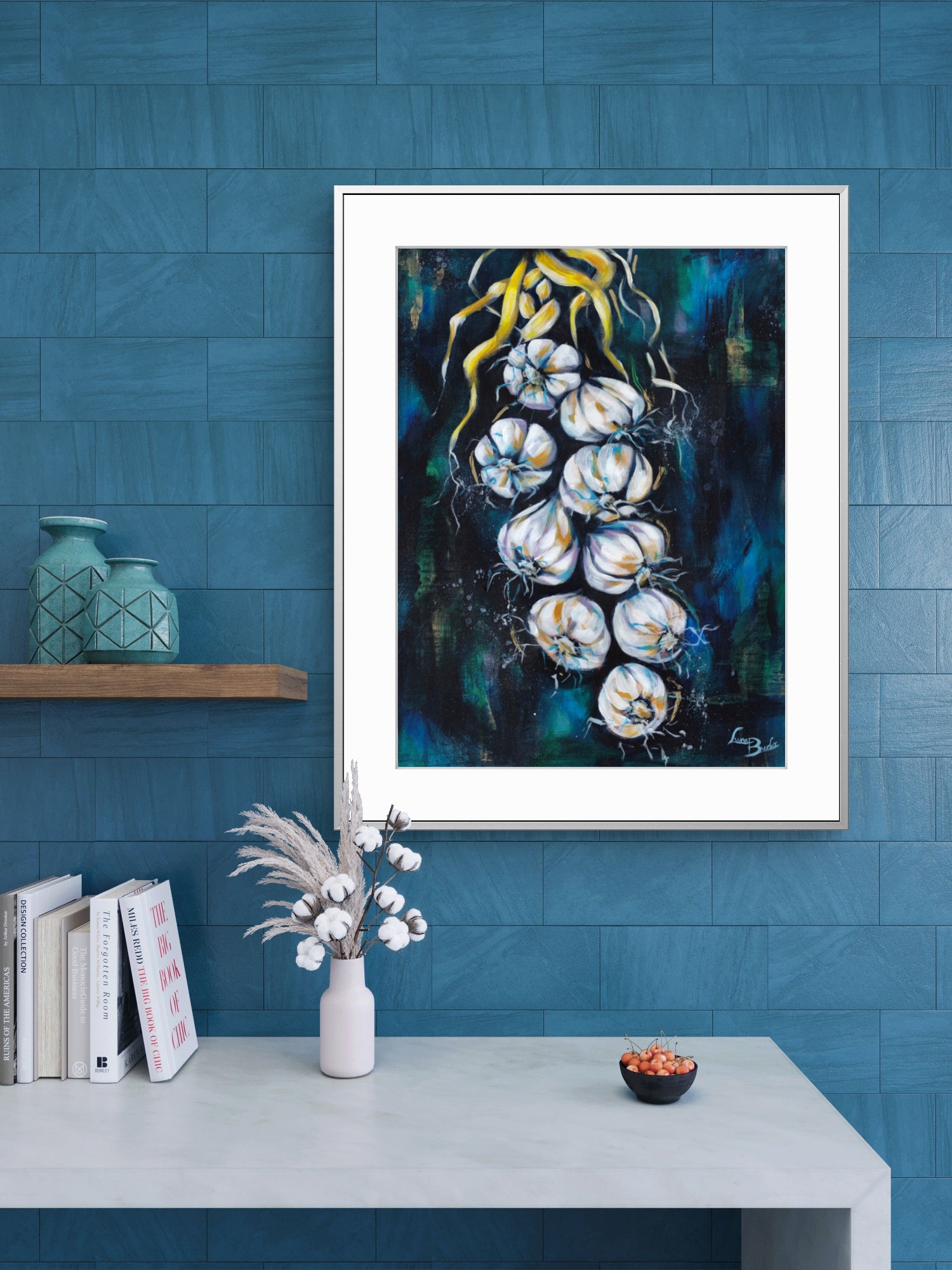 Framed Luna Burlo artwork of white garlic on a blue wall with decor items below