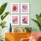 Four framed Luna Burlo kitchen artworks on a wall with a colorful vase, rainbow decoration, and plant in the foreground.
