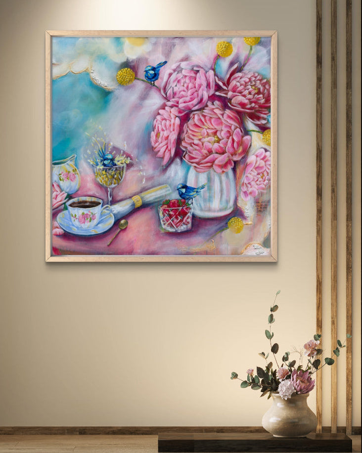 Framed painting of flowers, fairy wrens, and tea cups on a wall with a vase of flowers below.
