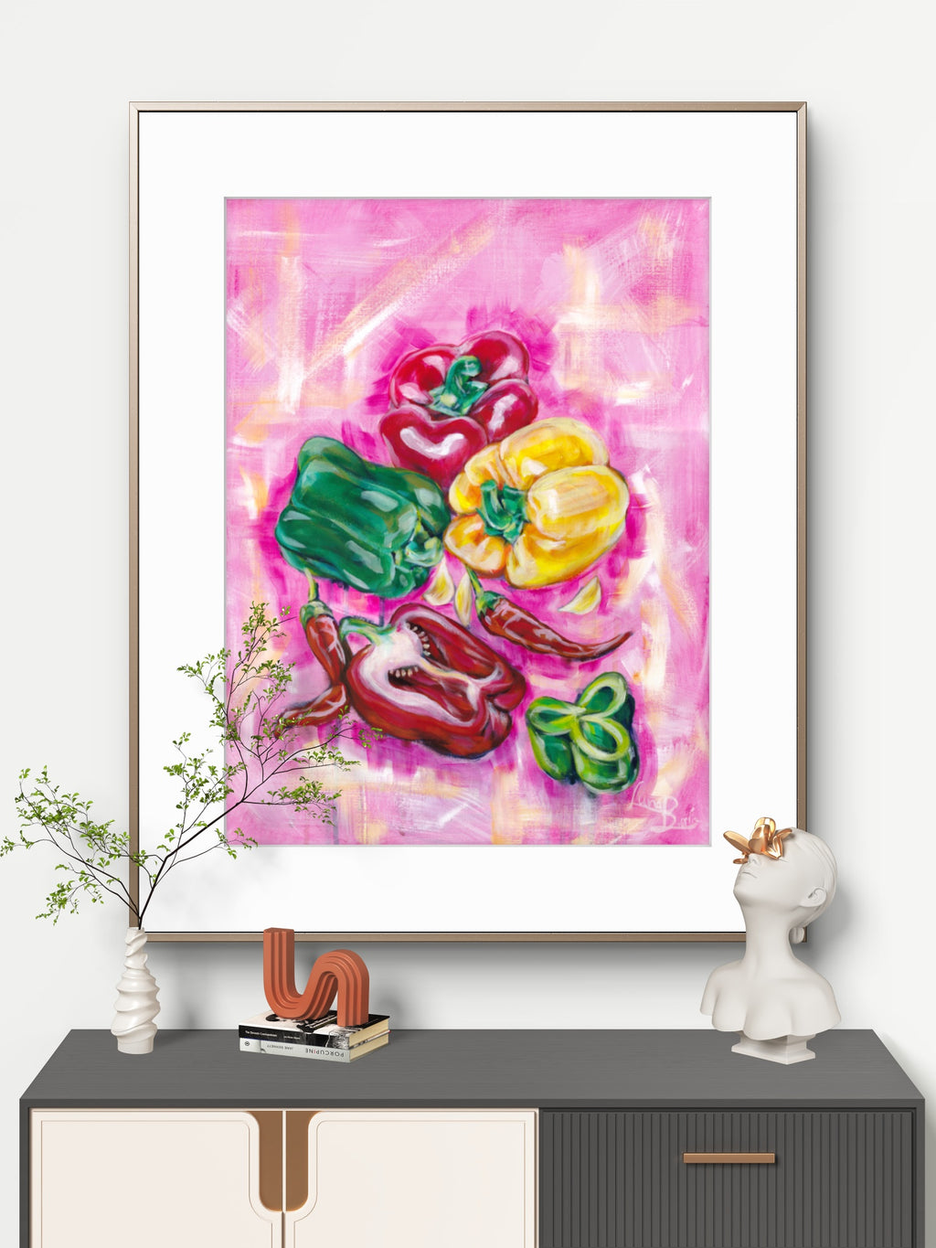 Framed abstract Luna Burlo artwork with colorful capsicum peppers on a pink background, displayed on a shelf.