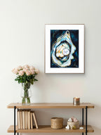 Framed Luna Burlo abstract art of an oyster on a wall above a wooden console table with decor items.