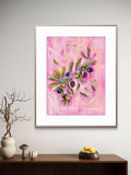 Framed Luna Burlo artwork with olives design on a pink background, displayed on a wall above a wooden shelf.