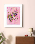 Framed Luna Burlo olives abstract artwork on a wall above a wooden dresser with a lamp and apples.