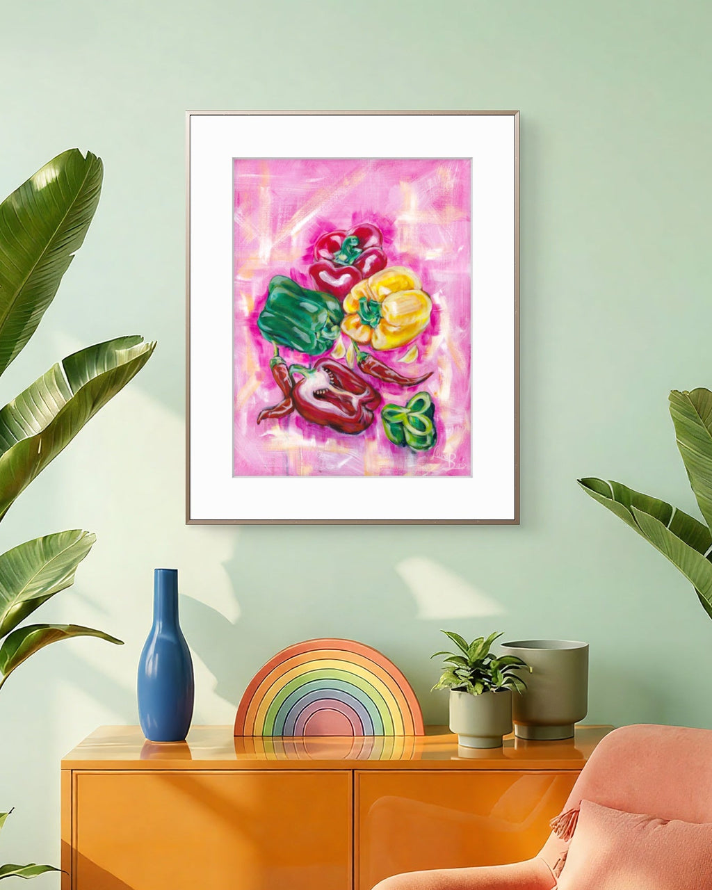 Framed Luna Burlo artwork of capsicums on a wall with a colorful rainbow, blue vase, and pink chair.