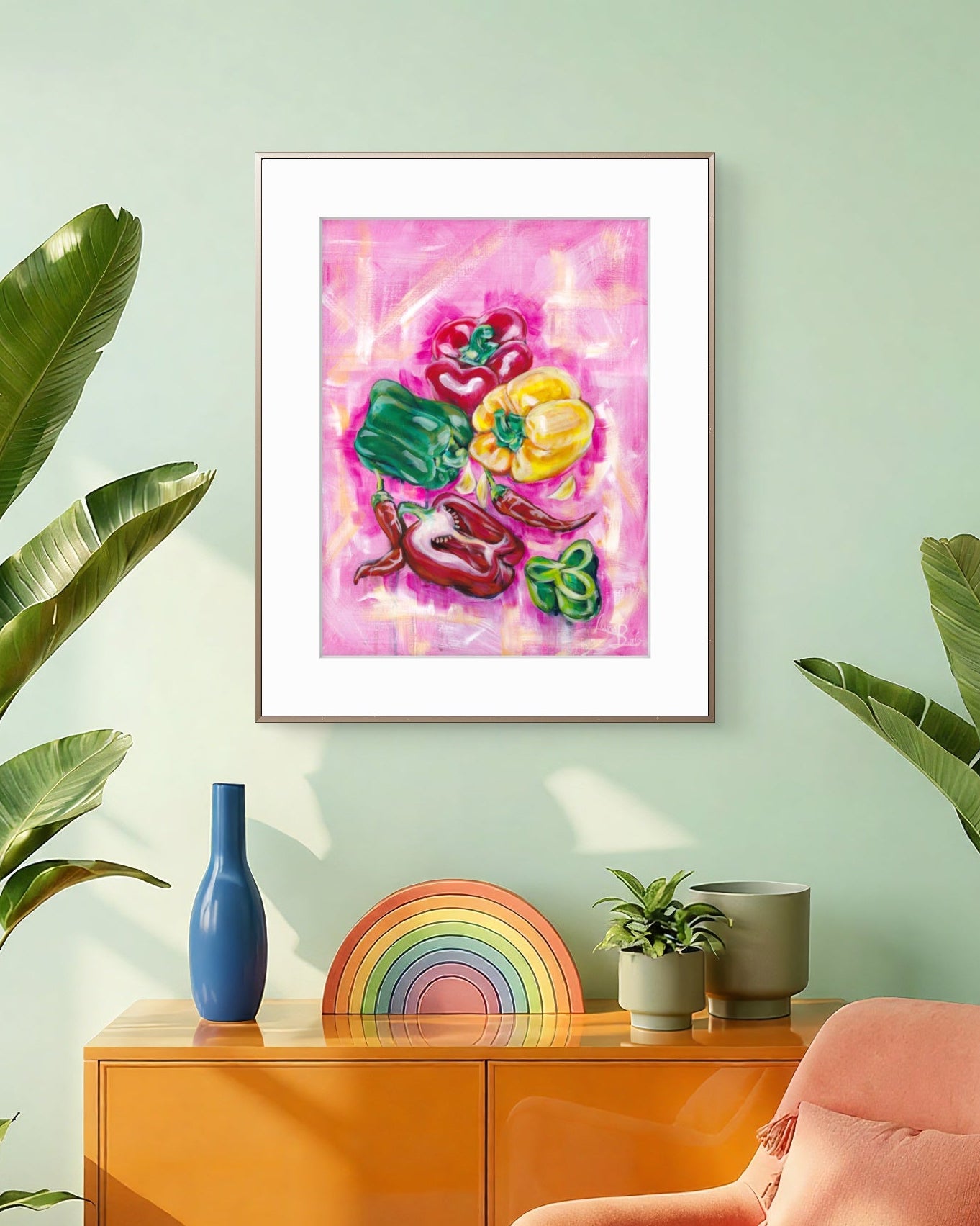 Framed Luna Burlo artwork of capsicums on a wall with a colorful rainbow, blue vase, and pink chair.