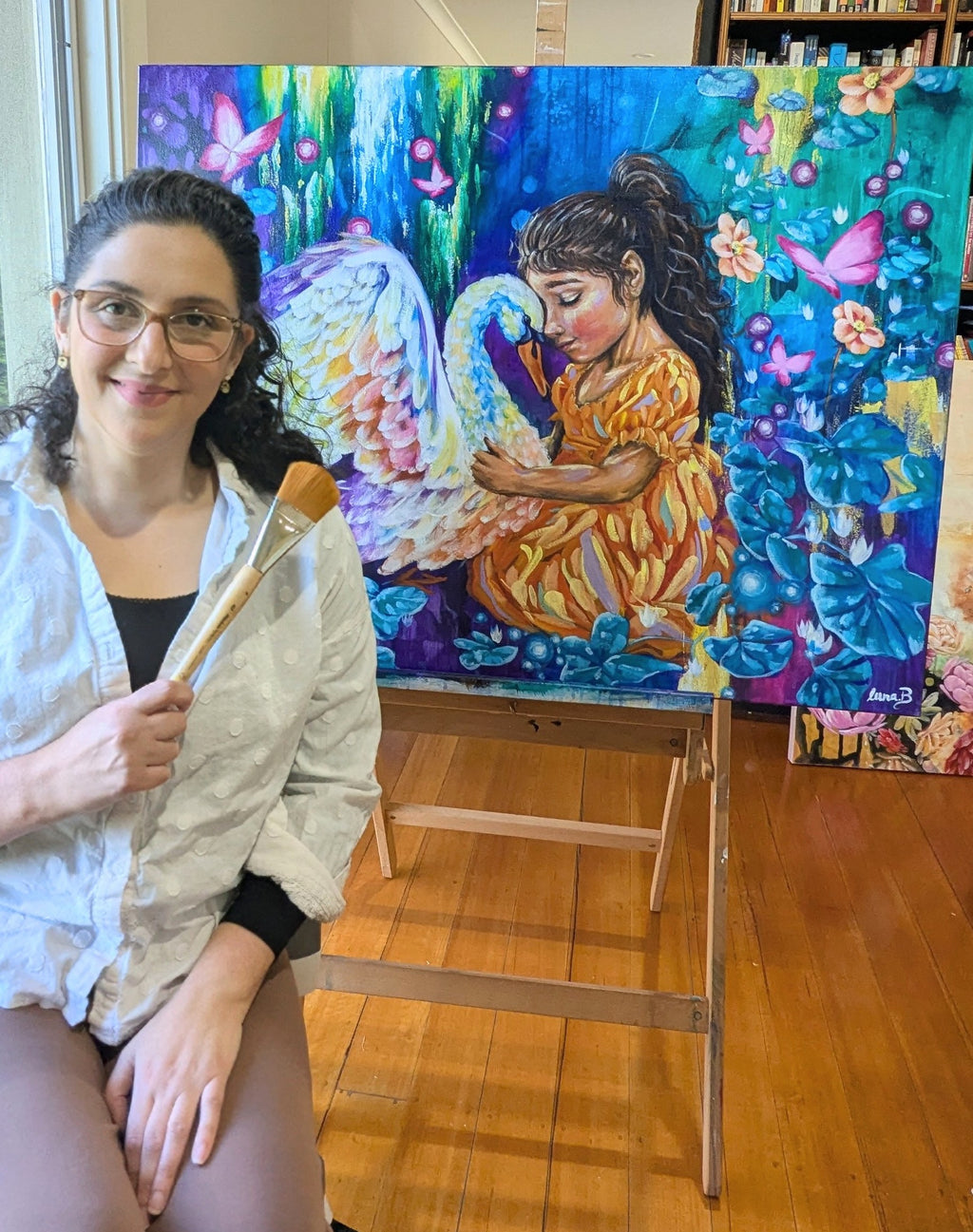Luna Burlo holding a paintbrush in front of a colorful painting of a woman with a child.