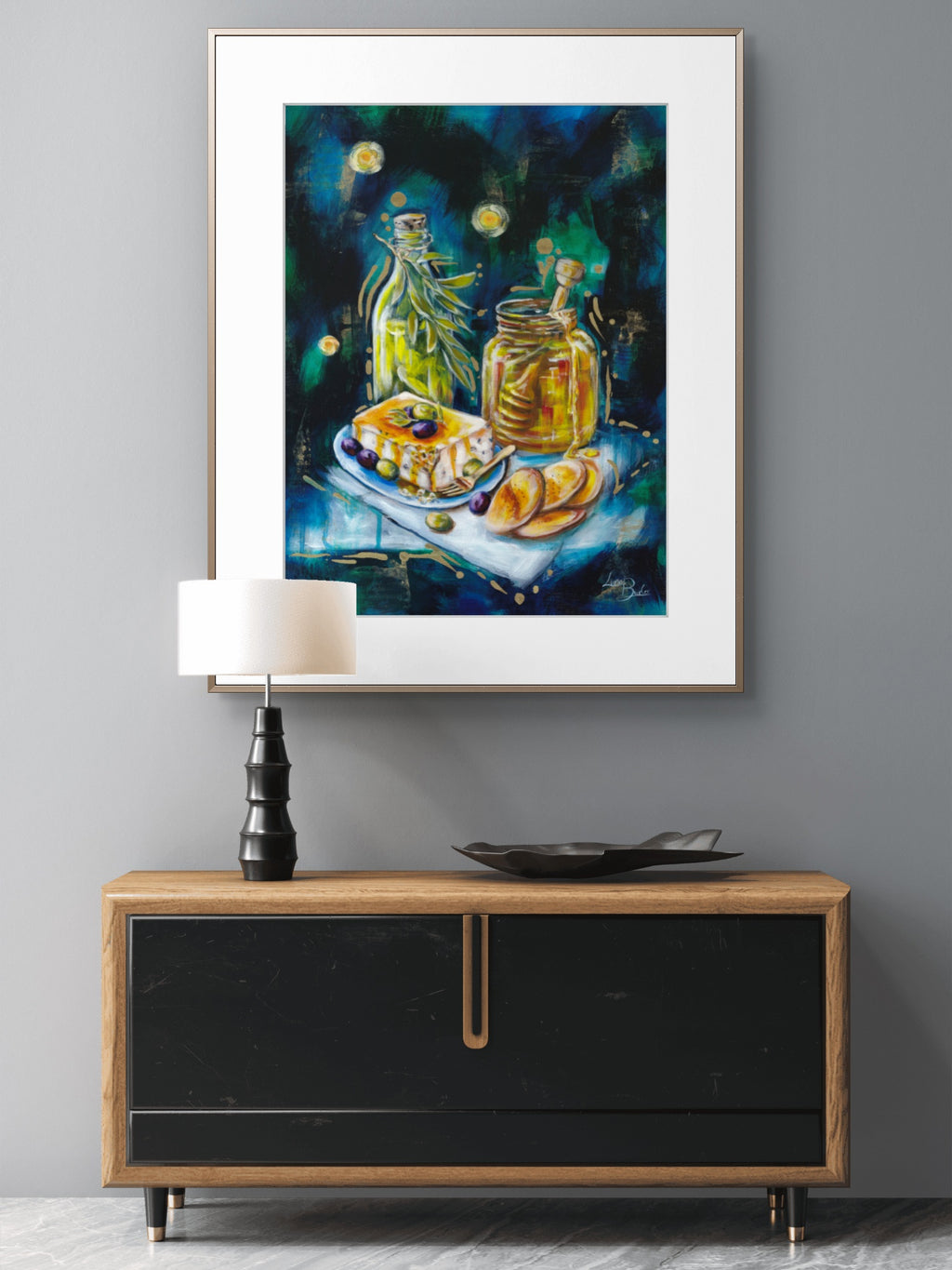 Framed painting of a Luna Burlo still life scene on a wall above a wooden cabinet.