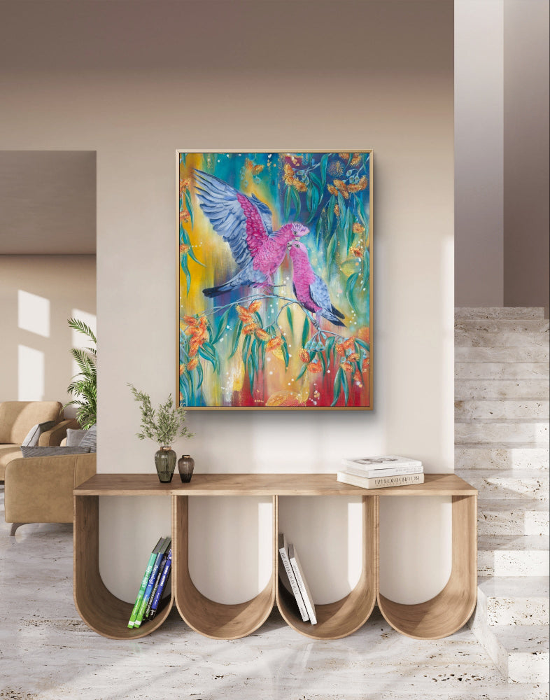 Colorful abstract fine art canvas print of a Luna Burlo painting of an Australian Native galah bird and gum tree flowers on a hallway statement wall above a wooden console table in a living room. Red, blue, yellow background, with rectangle vertical or tall portrait orientation. From Melbourne, Australia
