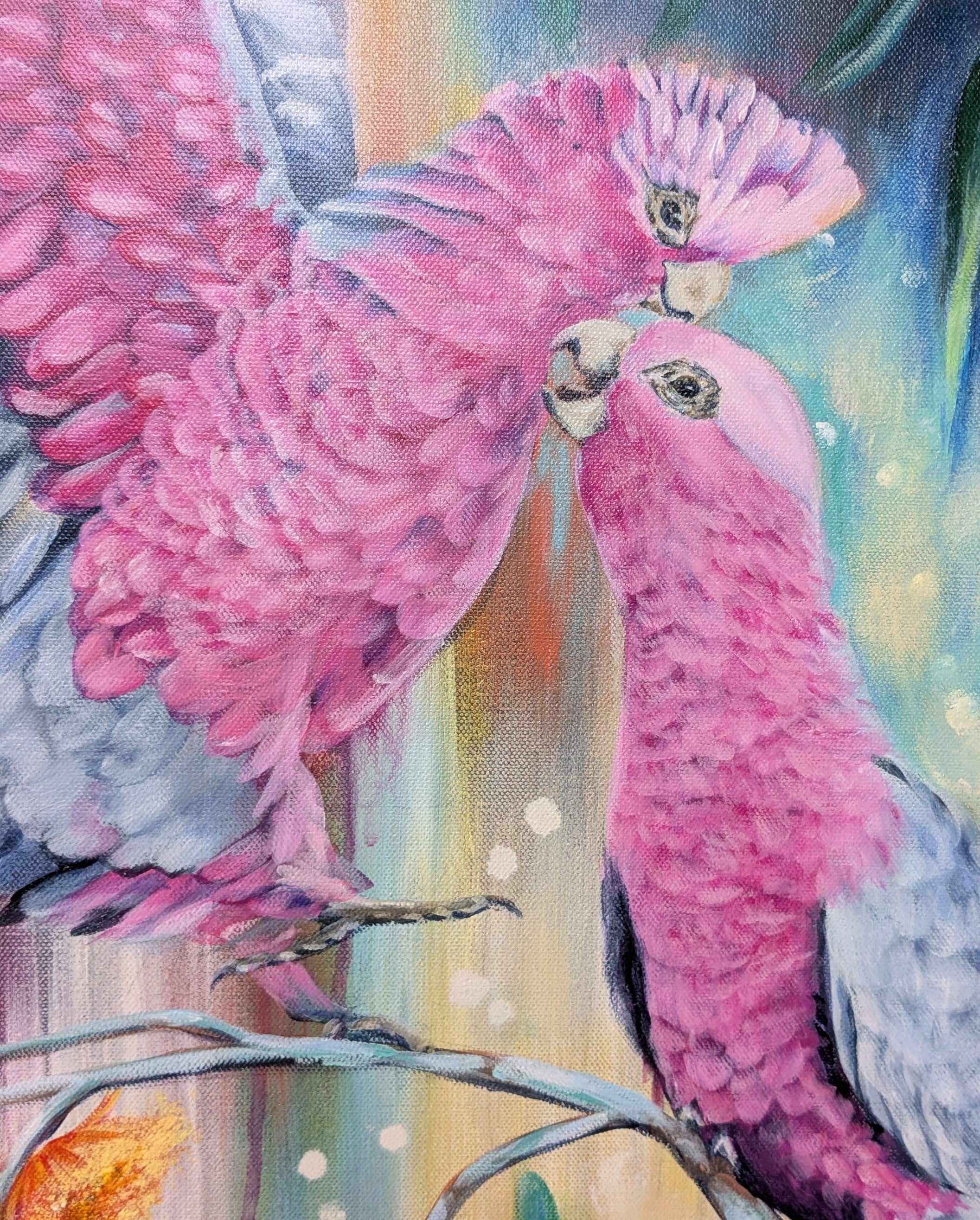 Large painting of two Australian pink galahs perched on a native plant, eucalyptus, branch with a colorful blue, gold, and orange background. Artist, Luna Burlo, Melbourne, Australia