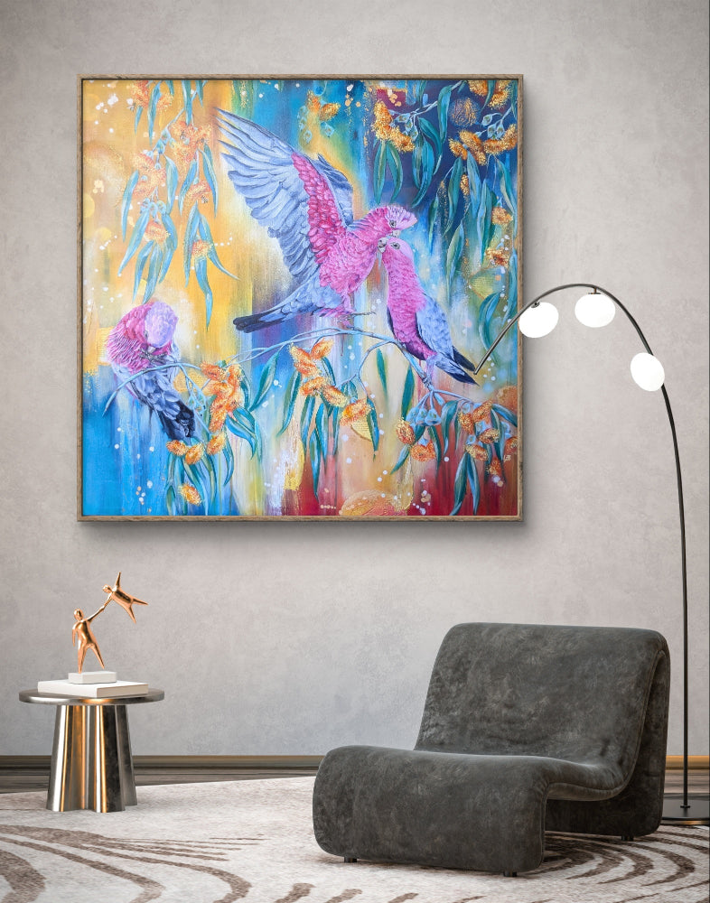 Large colorful abstract painting or fine art print of pink Native Australian galah birds and orange gum tree blossoms flowers on a modern living room wall above a gray armchair. Art by Melbourne art, Luna Burlo