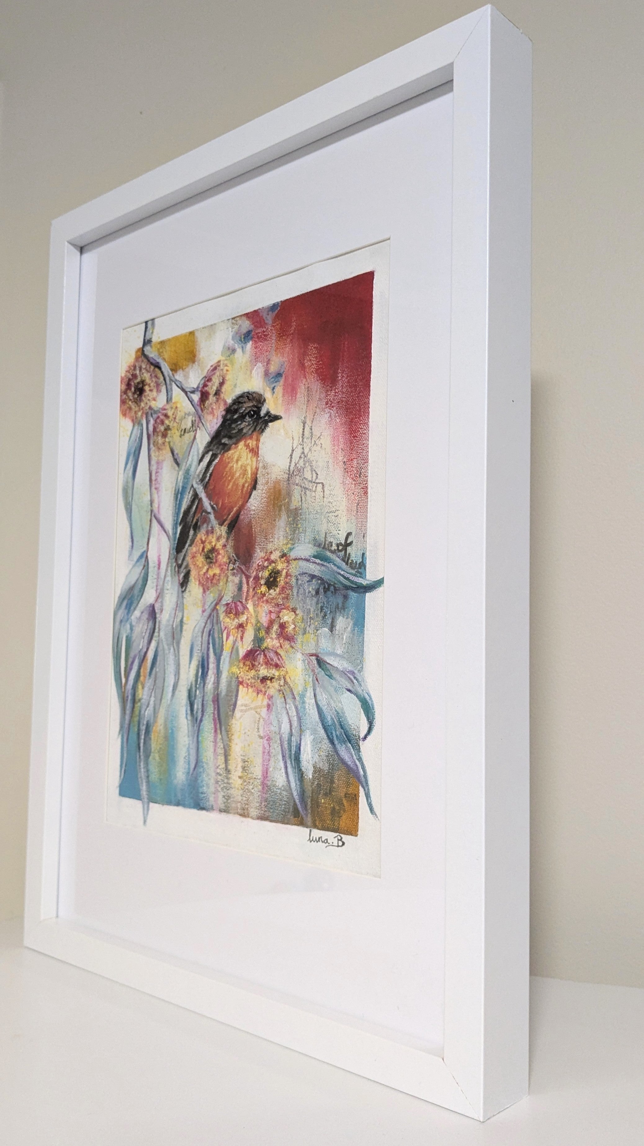 Framed artwork with a colorful depiction of a flame robin bird and abstract elements on a beige wall.