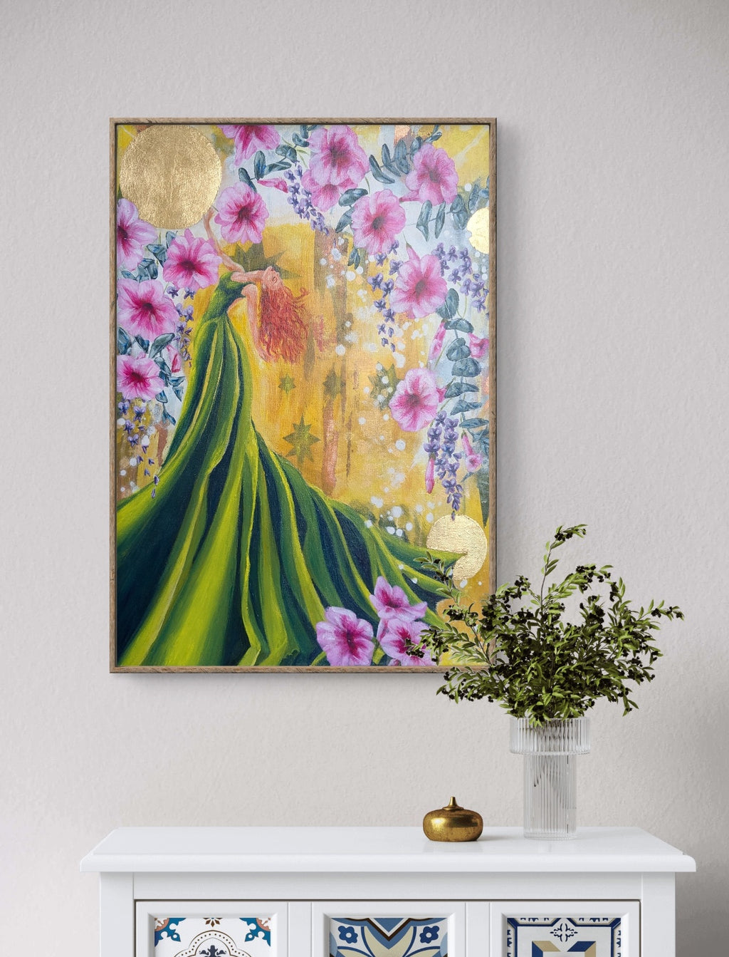 Framed Luna Burlo artwork of a woman in a green dress with flowers on a wall above a white cabinet.