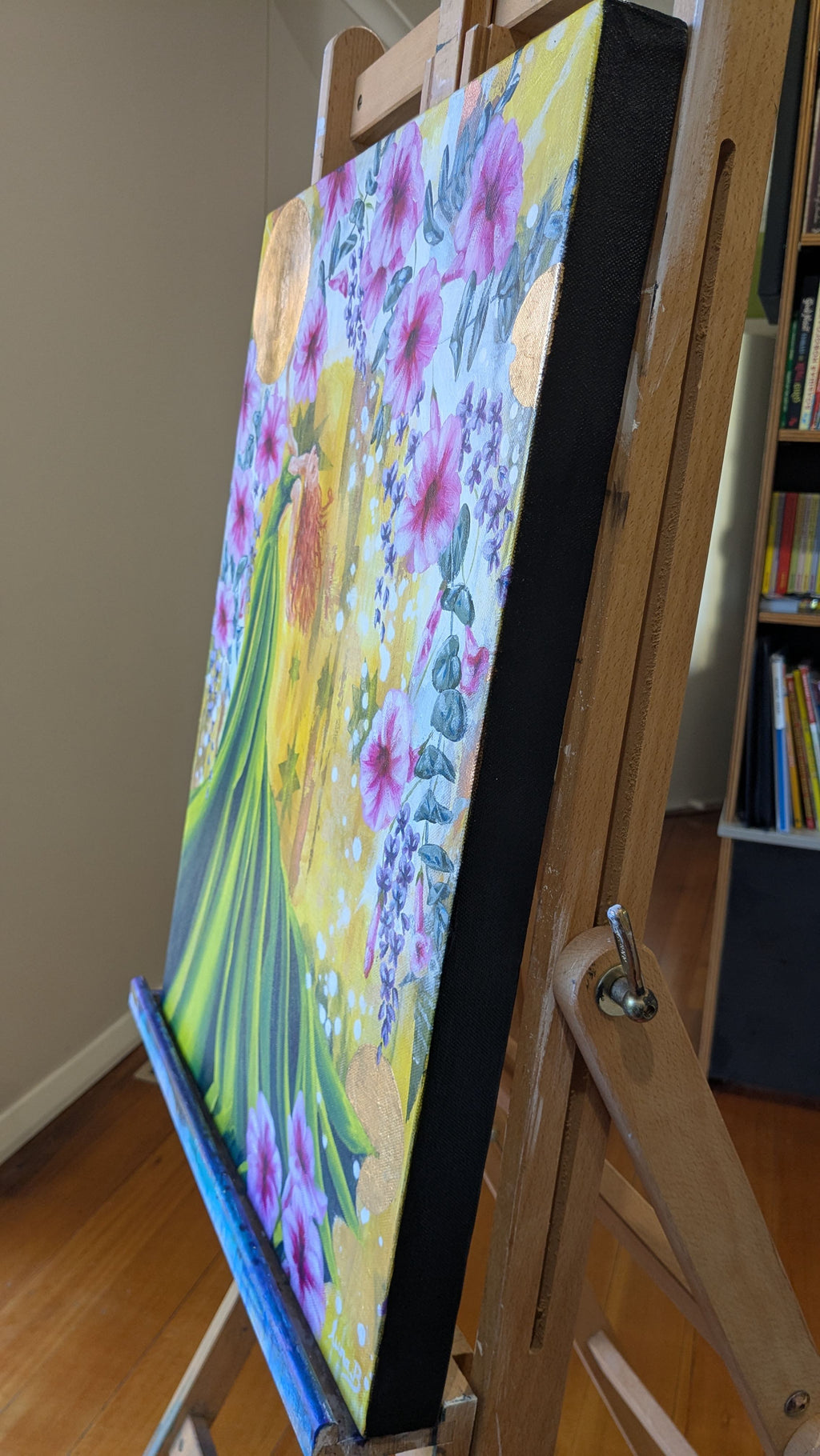 Luna Burlo Flourish colorful floral painting on an easel in a room with books.