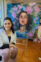 Artist, Luna Burlo, sitting in front of her colorful painting, "July in Bloom", which depicts a woman's face with lotus and lukspur flowers. July birth month flowers and constellations for Leo and Cancer star signs / zodiac. In Melbourne, Australia