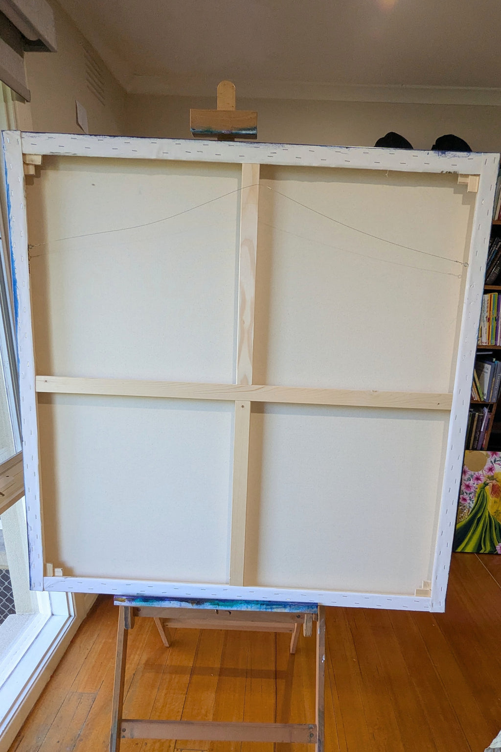 Large white canvas on an easel in a room with books and a window, from July in Bloom, by artist: Luna Burlo, Melbourne