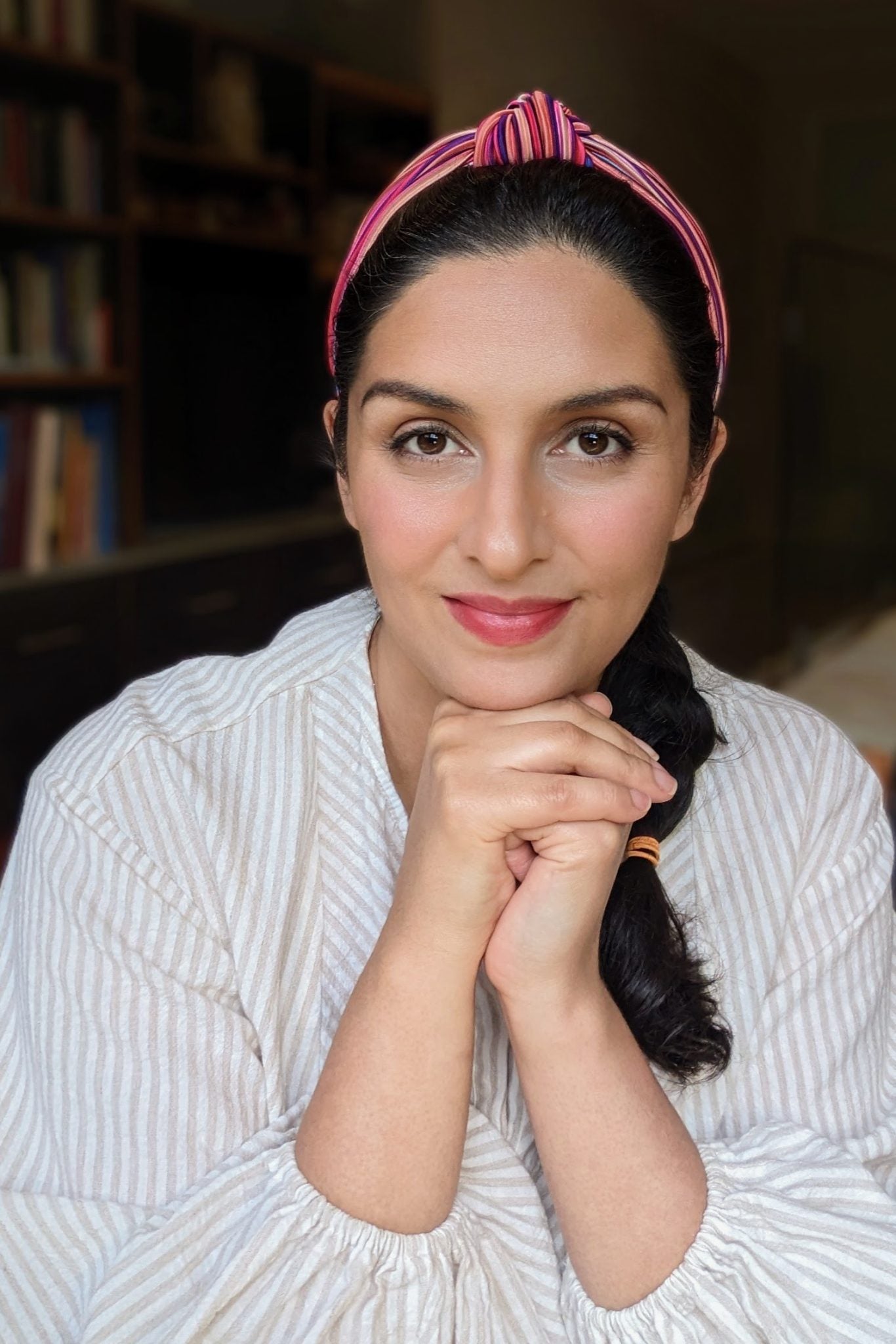 Luna Burlo artist with a pink headband and white shirt sitting in front of a bookshelf.